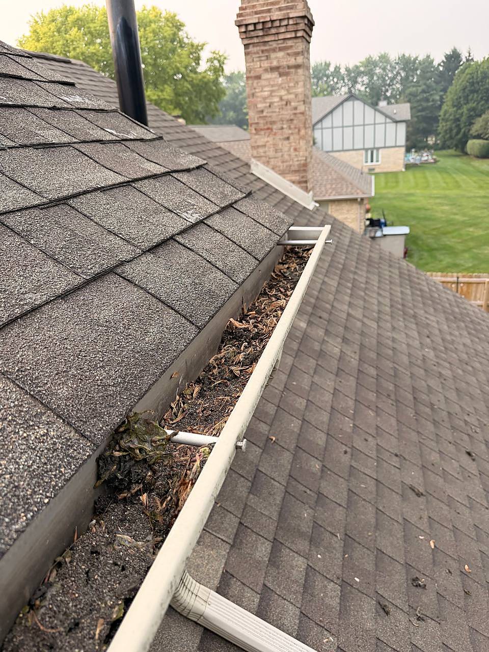 Gutter filled with wet leaves and grit beside the chimney before gutter cleaning in Shelby Township